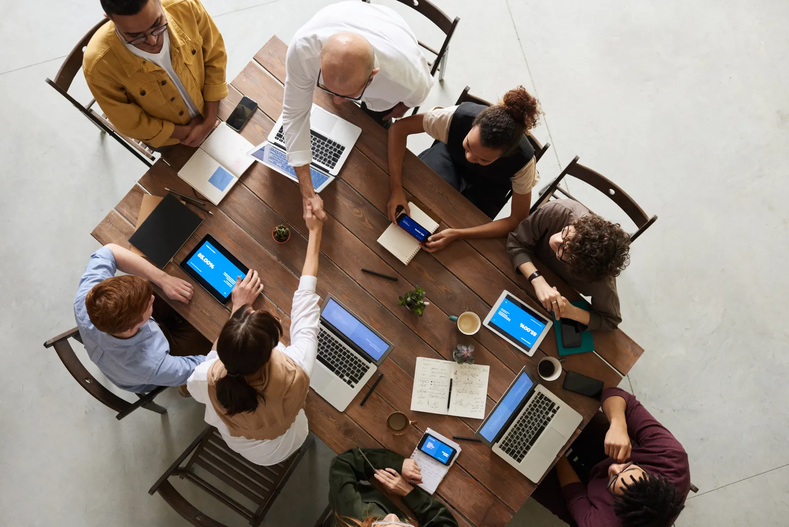 Vista cenital de un equipo trabajando alrededor de una mesa con computadoras portátiles y documentos