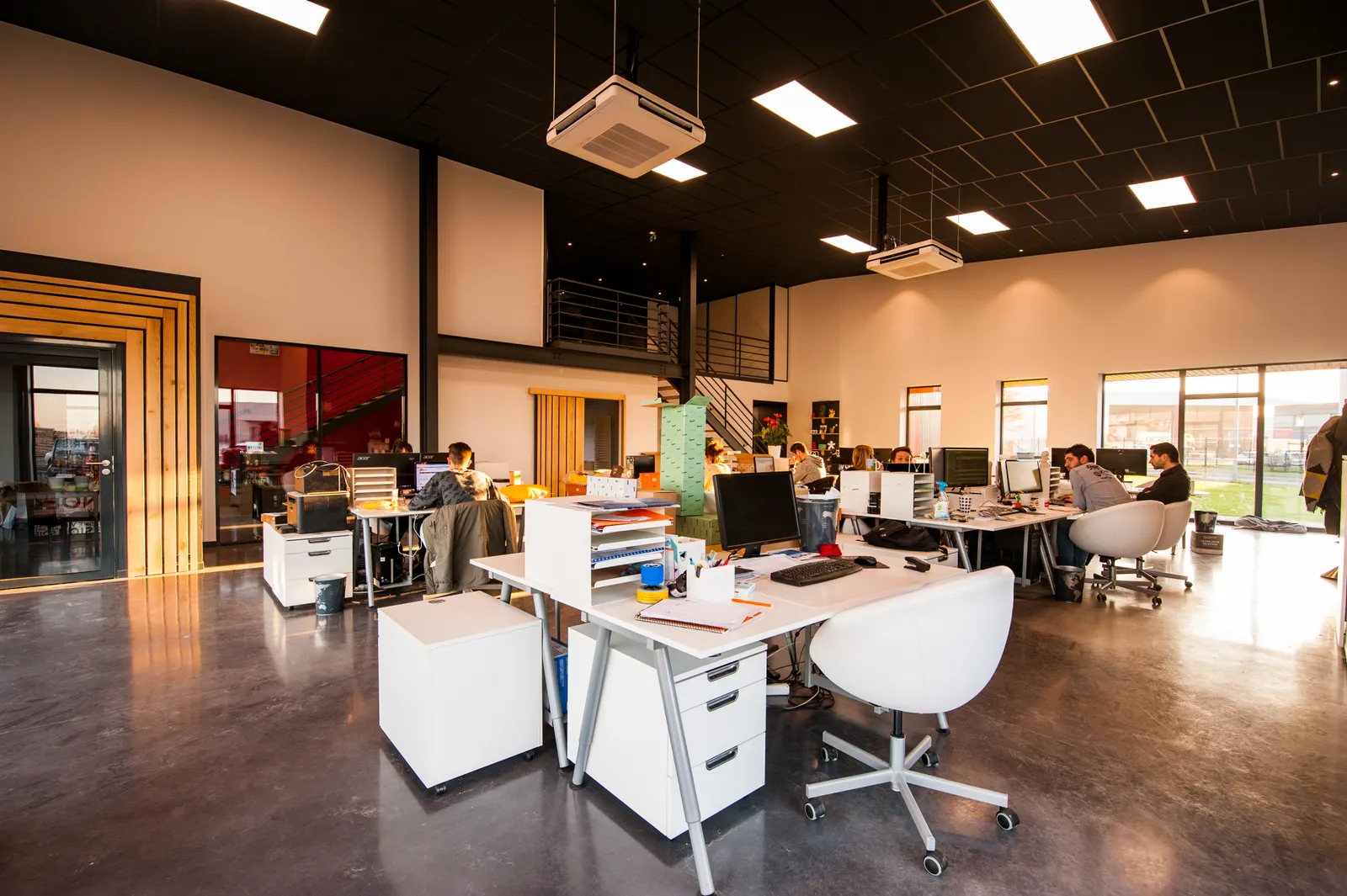Oficina abierta y luminosa con escritorios y personas trabajando al fondo
